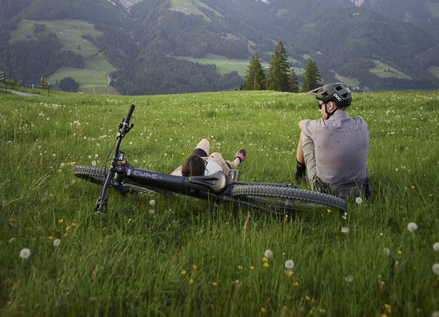 Two people in a meadow in Leogang, with a bike lying nearby.