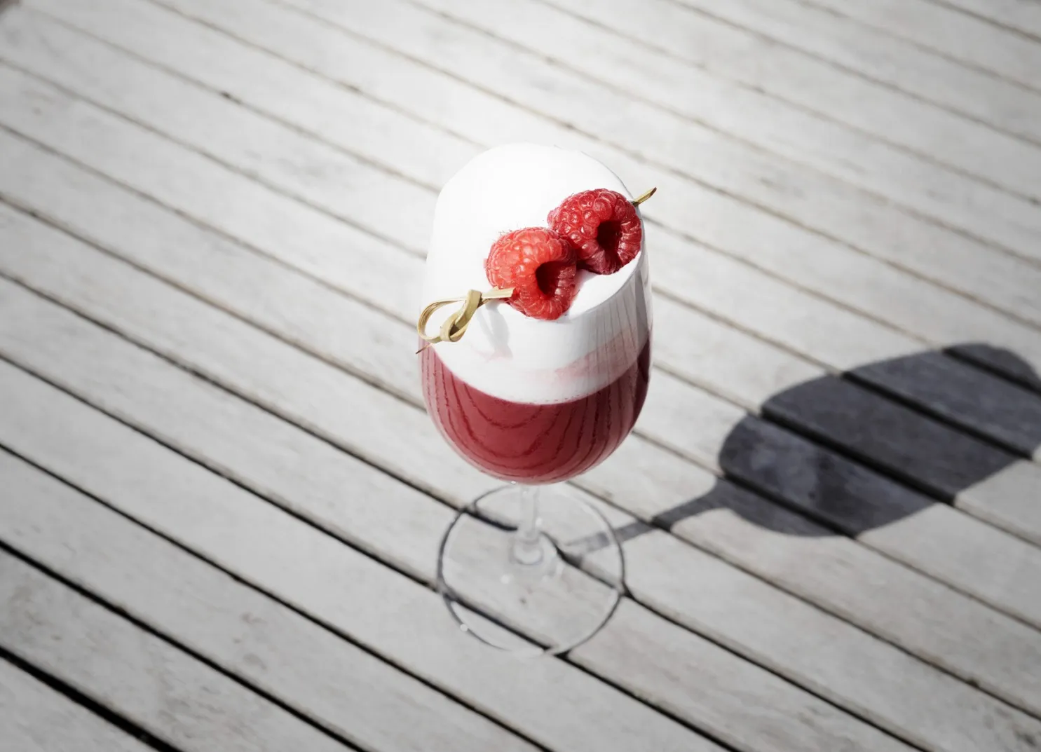 Dessertgetränk in einem Glas mit Himbeer-Garnitur auf einer Holzoberfläche