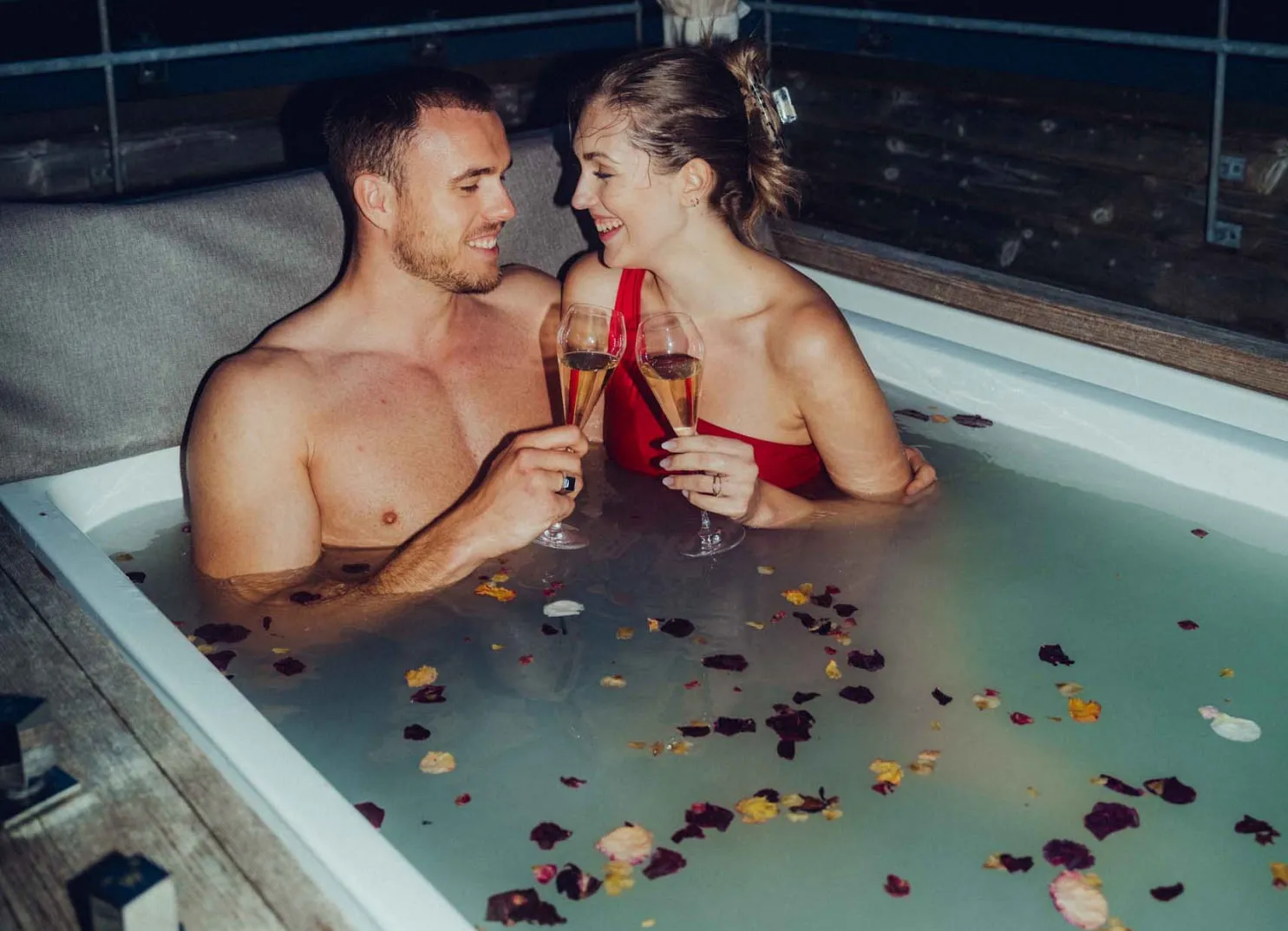 Paar im Whirlpool mit Sektgläsern und Blumenblättern