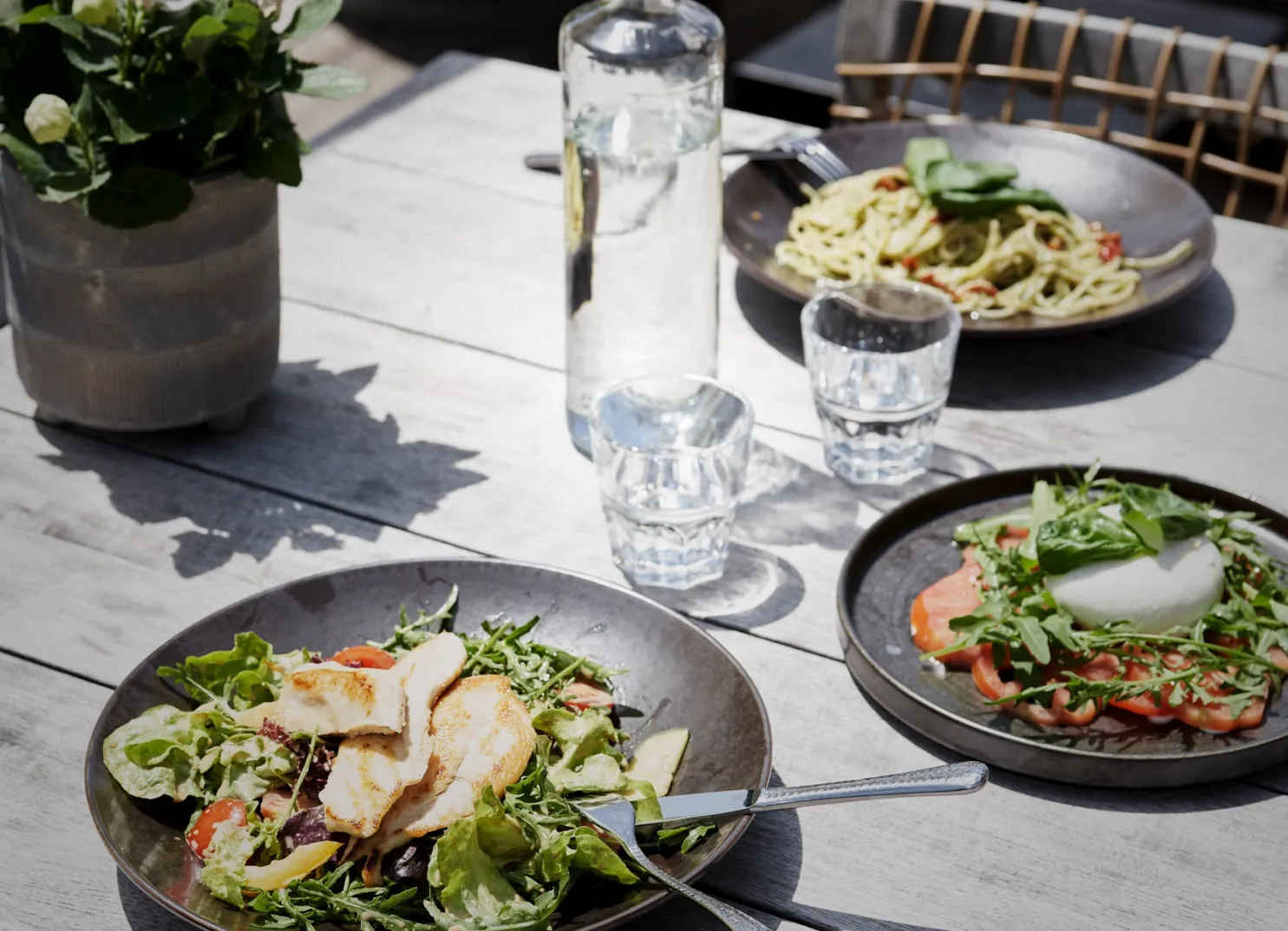 Teller mit Salat und Pasta sowie Getränken auf einem Holztisch
