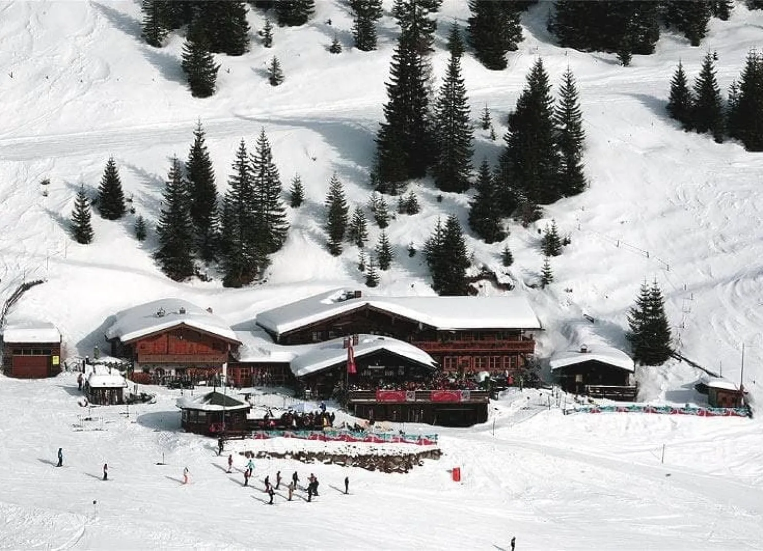 Hütte in verschneiter Landschaft mit Skifahrern und Bäumen