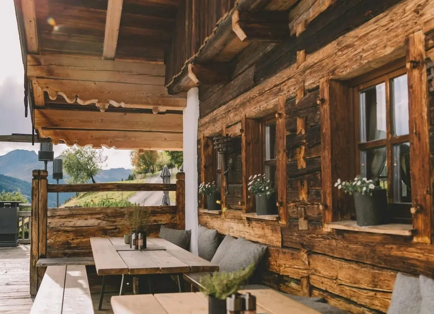Außenansicht einer Holzhütte mit Tischen, Bänken und Blumenkübeln