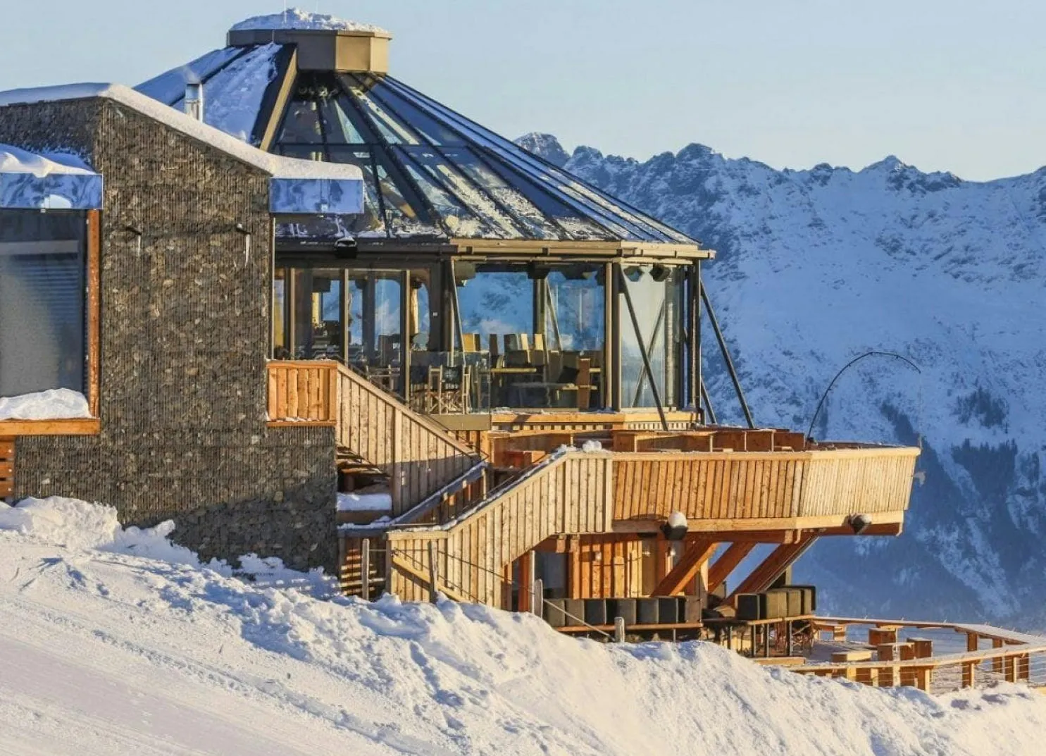 Modernes Restaurant mit Glasdach, umgeben von schneebedeckten Bergen