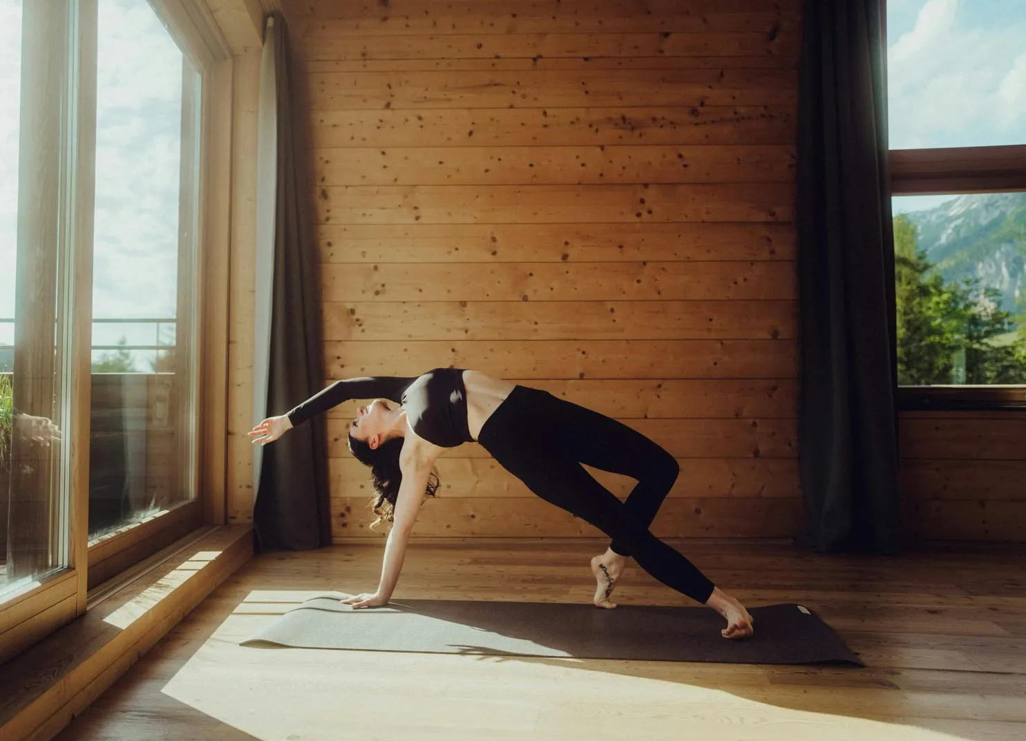 Frau macht Yoga in einem hellen Holzraum mit großen Fenstern