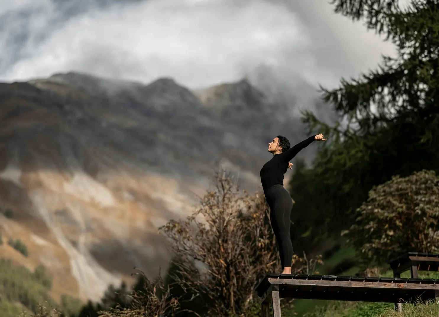 Person, die sich auf einer Holzplattform mit Bergen im Hintergrund dehnt
