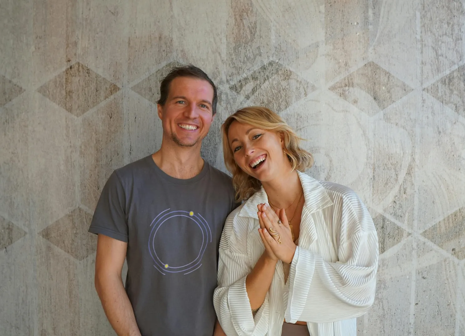 Ein Mann und eine Frau stehen lächelnd vor einer dekorativen Wand.