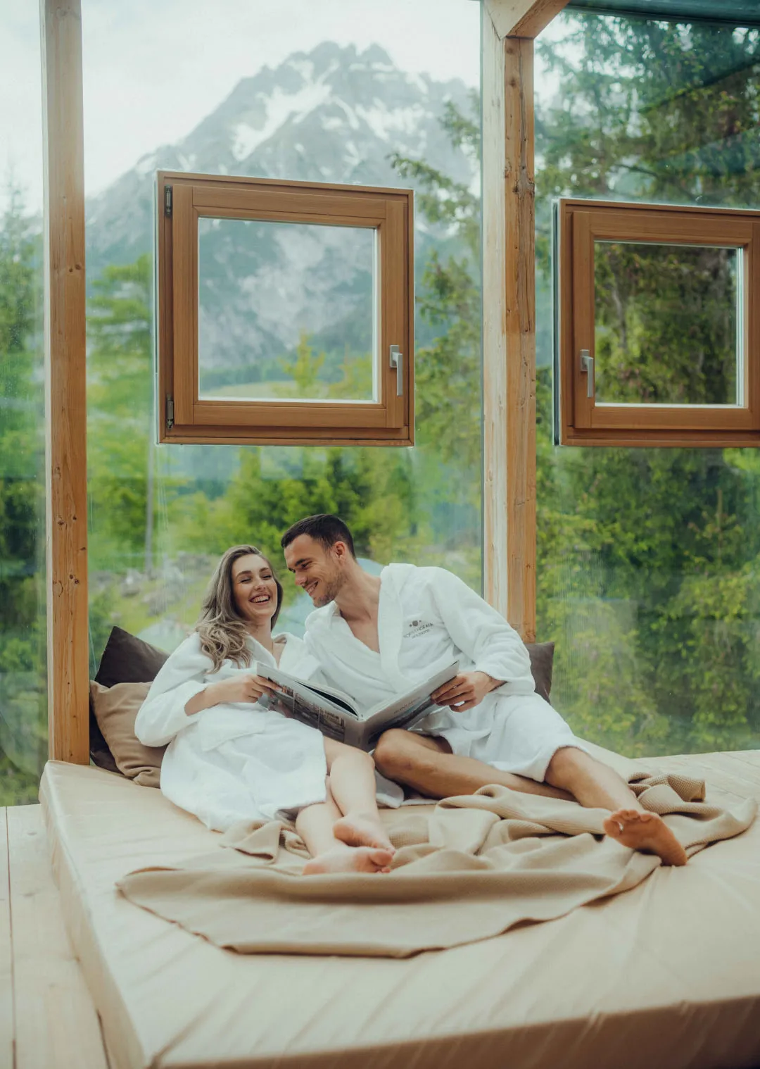 Couple in bathrobes sitting on a bed with mountain view