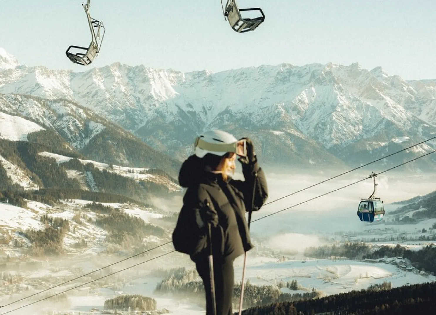 Person mit Hut in der Nähe einer Seilbahn in einer schneebedeckten Berglandschaft