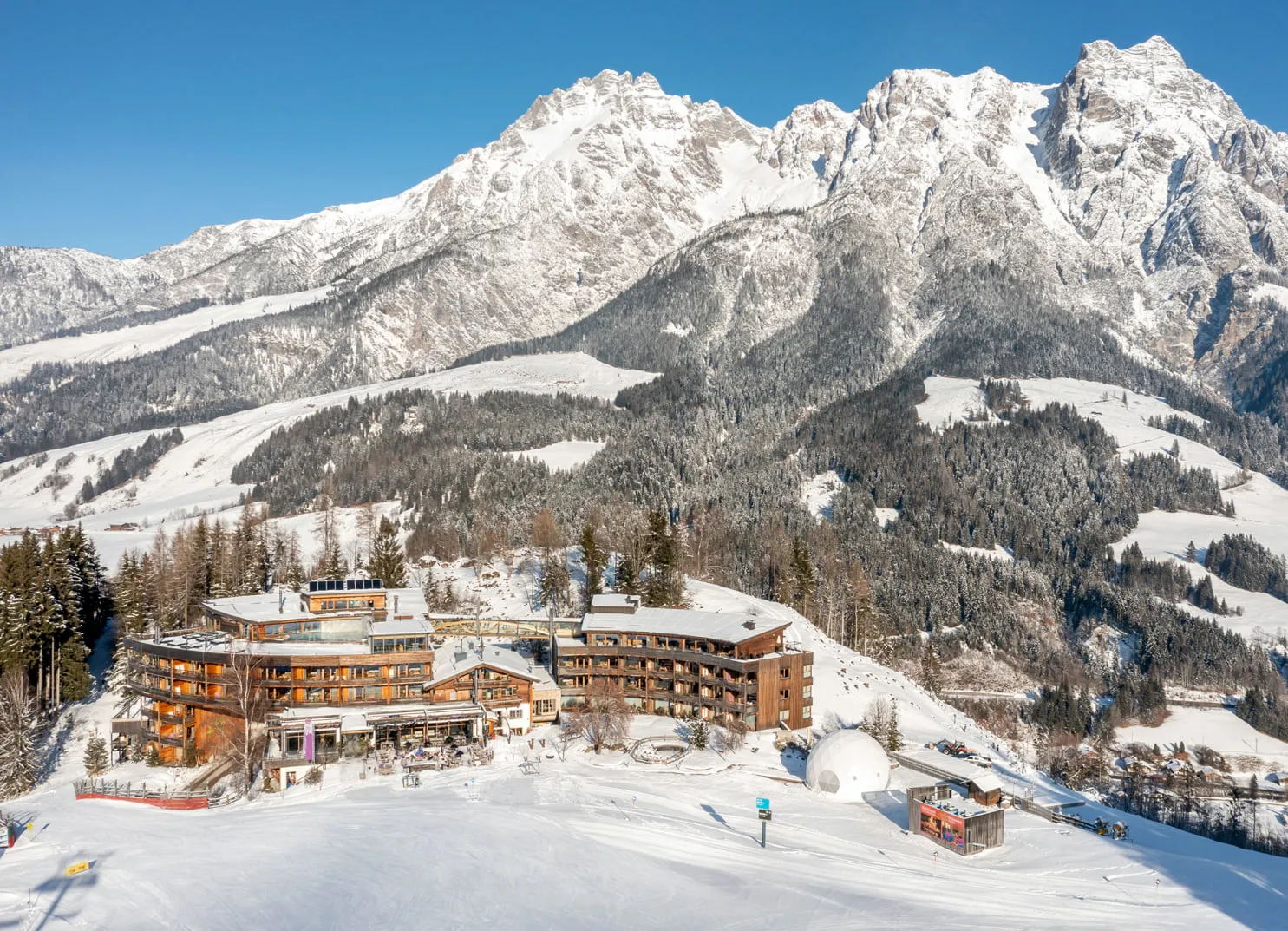 Luftaufnahme eines Hotels in einer verschneiten Berglandschaft.