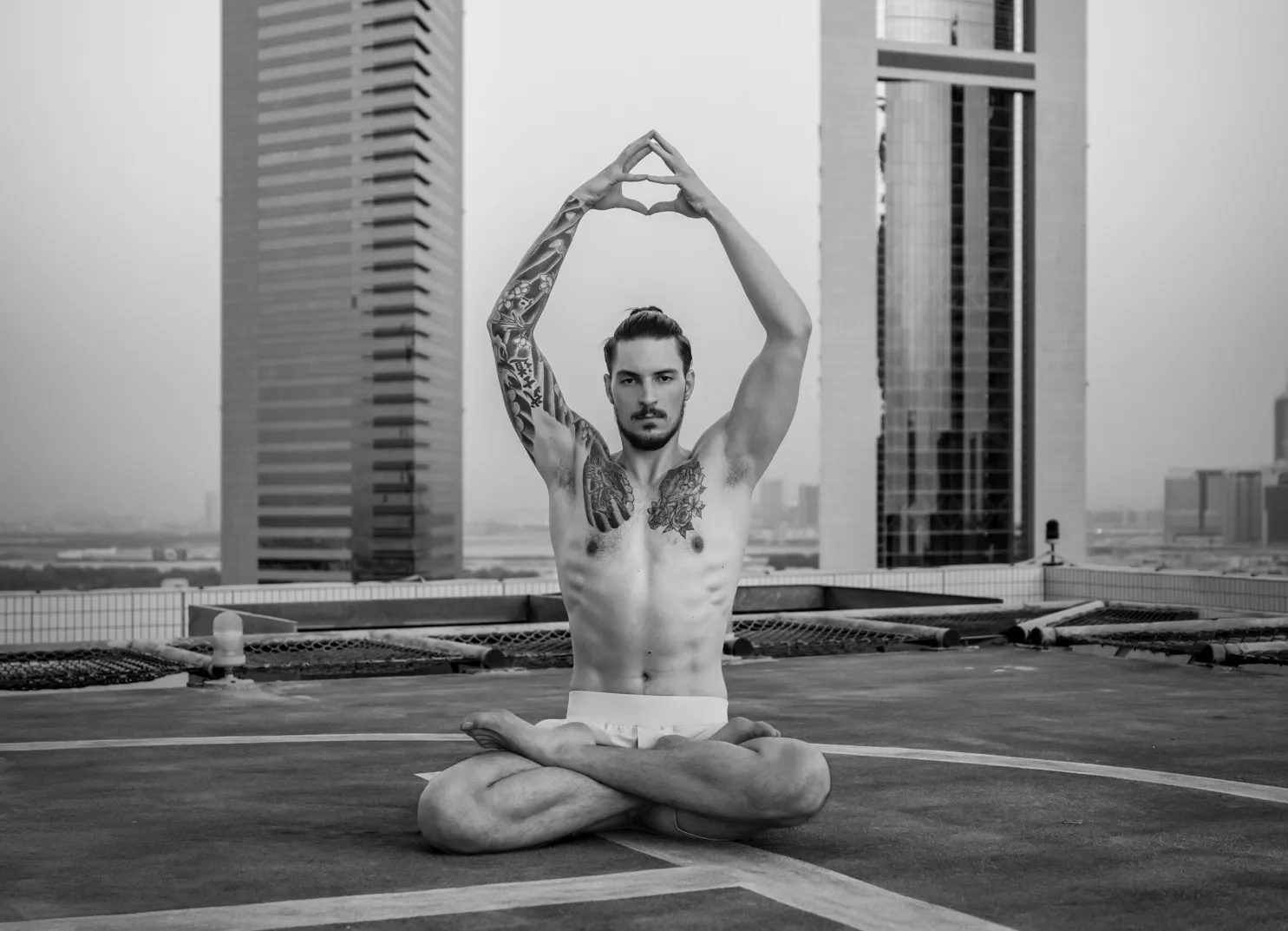 Ein Mann praktiziert Yoga auf einem Dach mit Wolkenkratzern im Hintergrund.