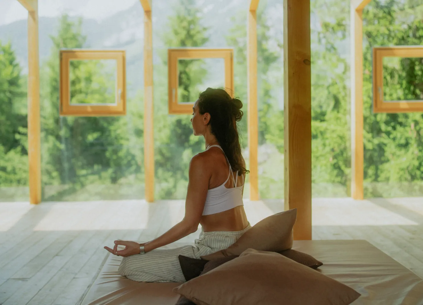 Frau meditiert in einem ruhigen Raum mit großen Fenstern und Grün draußen