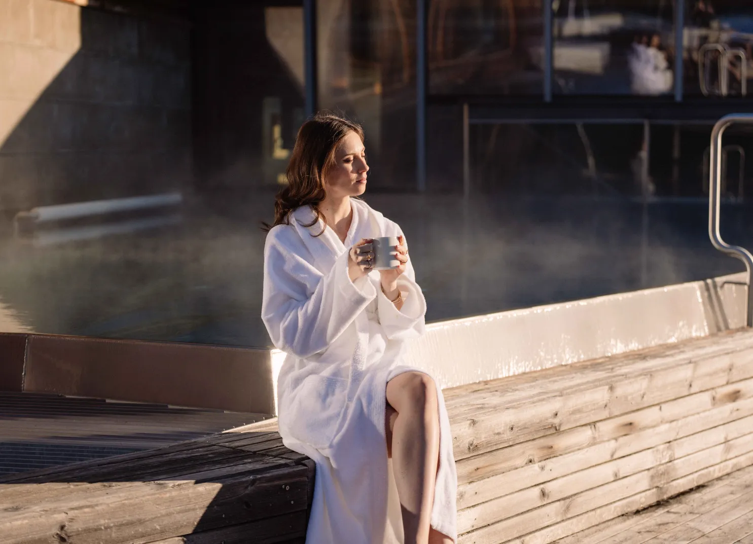 Frau in Bademantel sitzt am Spa mit einer Tasse in der Hand