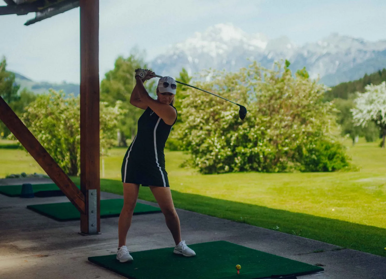 Frau schwingt Golfschläger auf Driving Range mit Bergen im Hintergrund