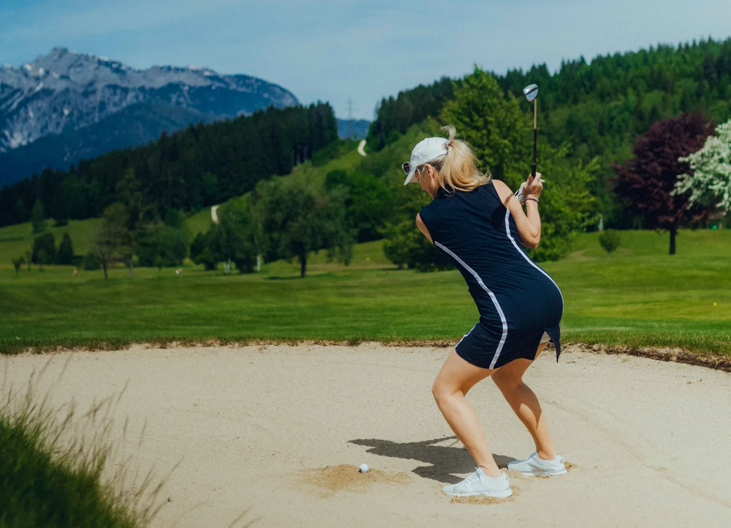 Woman in golf dress hits from sand bunker, mountains in the background