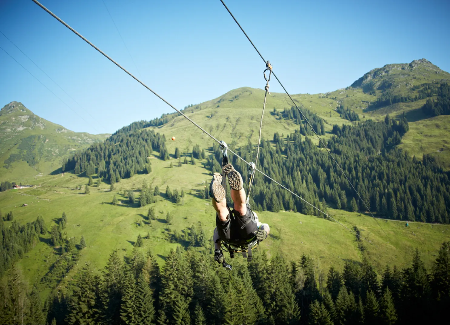 Person zip-lining over green hills