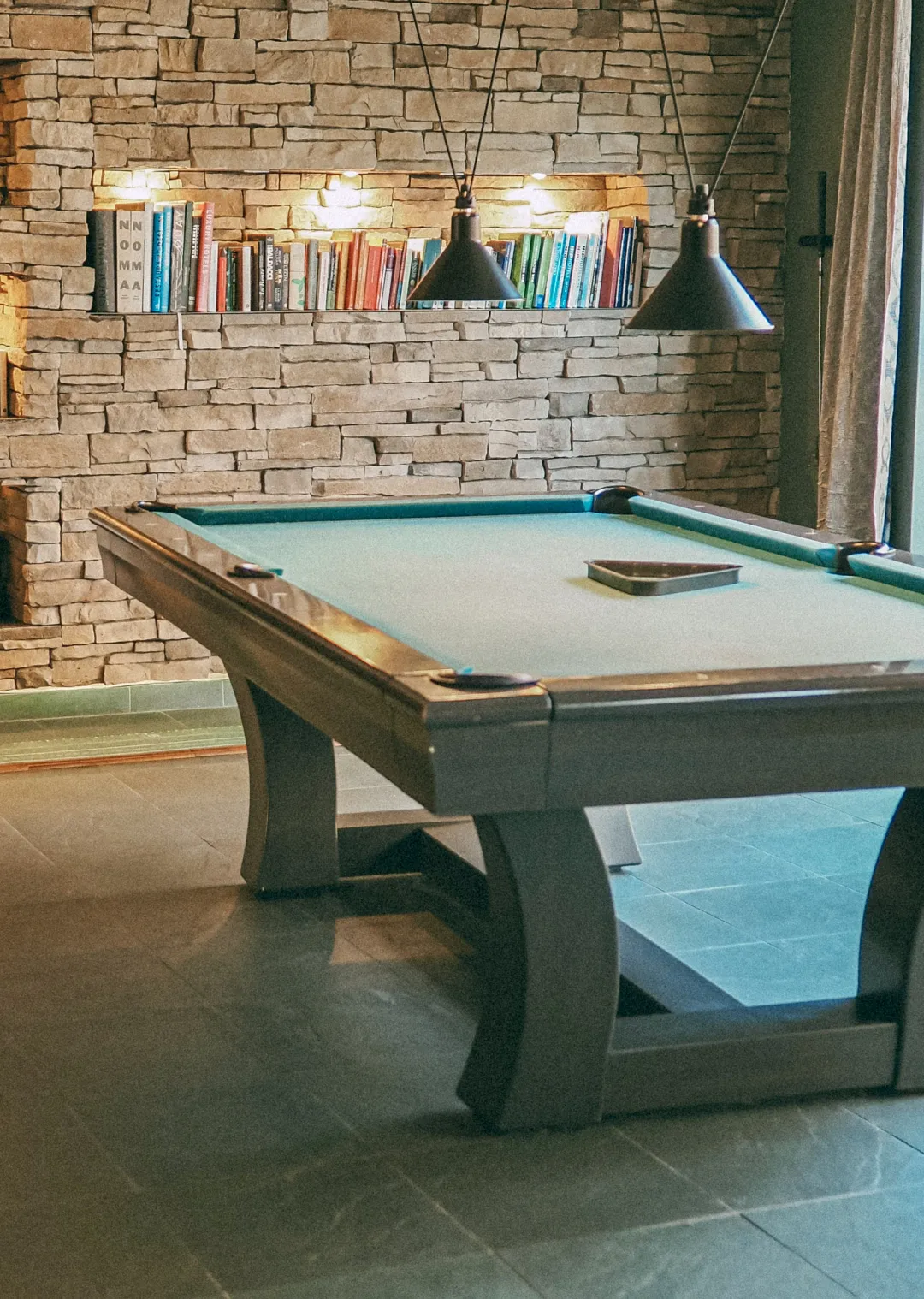 Pool table in front of a stone wall with bookshelves