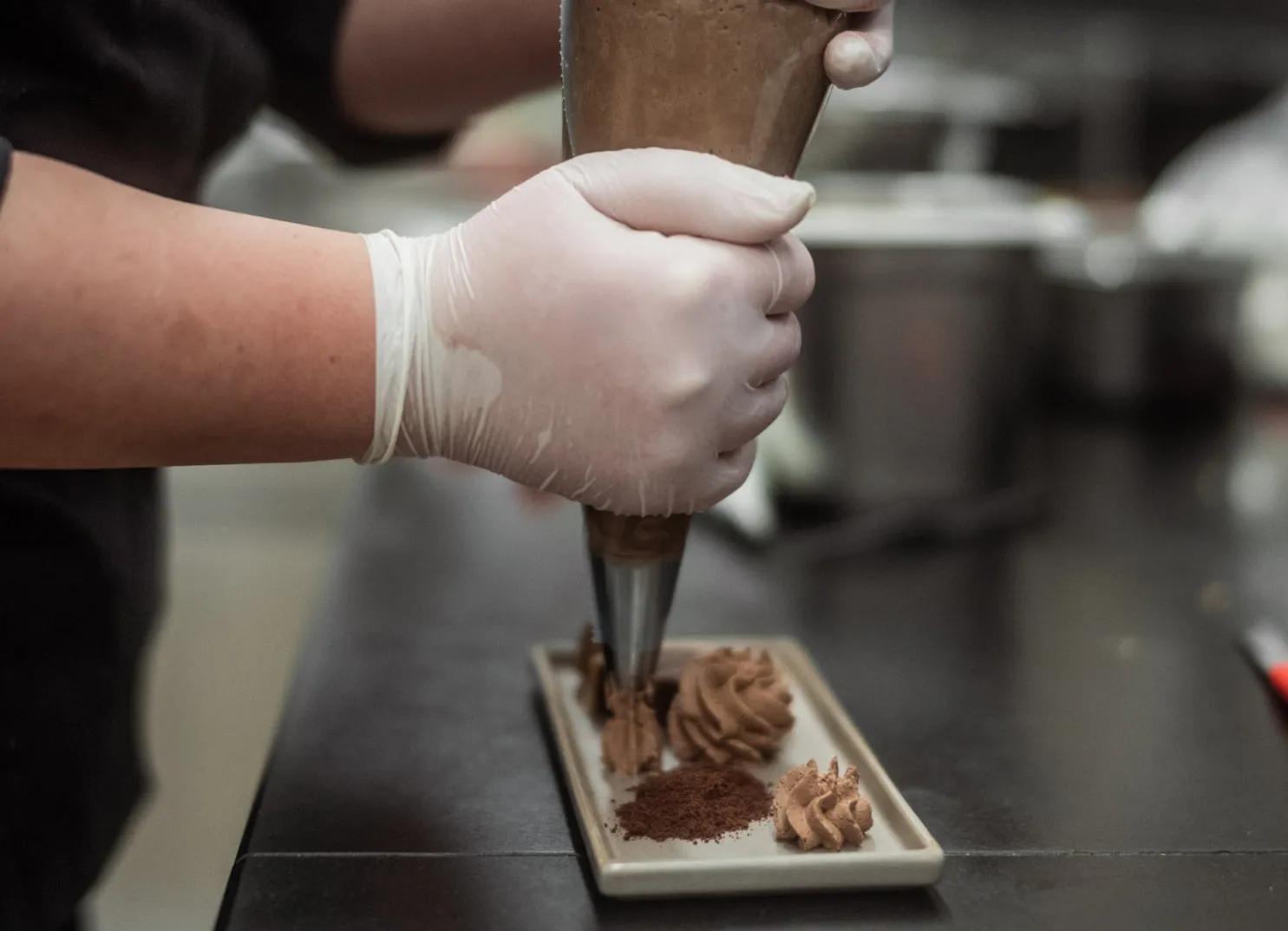 Piping dessert filling onto a plate in a restaurant kitchen